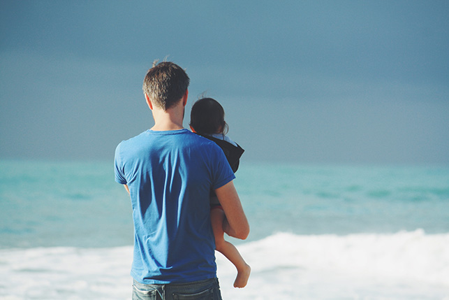 Dad holding daughter looking at ocean waves